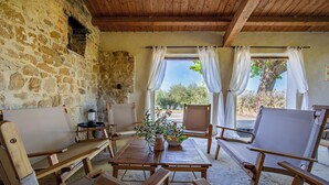 Un interno rustico con pareti in pietra, mobili in legno e vista all'esterno attraverso delle tende.