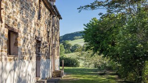 Un edificio in pietra dal design tradizionale, un vialetto erboso che conduce all'ingresso e un paesaggio collinare sullo sfondo.