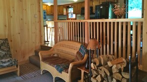 Ein gemütliches Blockhaus-Interieur mit einer Korbsesselcouch, einer Lampe und einem Holzstoß.