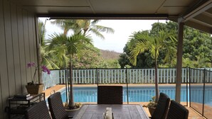 A covered patio with a pool, wicker furniture, and a view of the surrounding greenery.