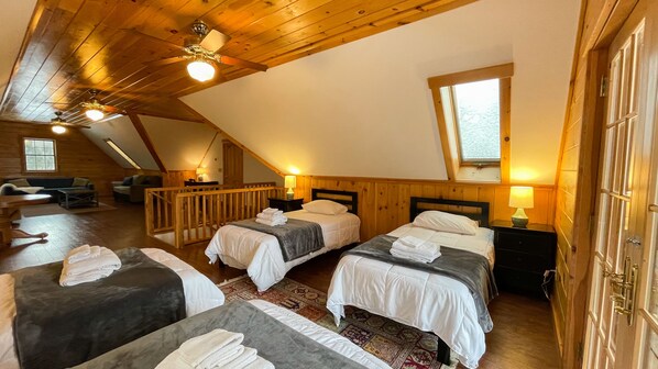A cozy attic bedroom with two beds, wooden beams, a sloped ceiling, and a large window. - The MOST private, beautiful Log Home for up to 12 guests. 10 min to Dreams Park (Hartwick)