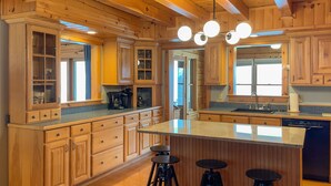Une cuisine spacieuse avec des meubles en bois, un îlot central doté de tabourets et une grande fenêtre qui laisse entrer la lumière naturelle.