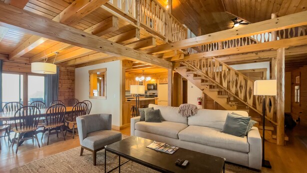Un vaste espace de vie doté d’un haut plafond, de poutres en bois, d’un canapé, d’une table basse et d’un coin repas avec des chaises et une table.