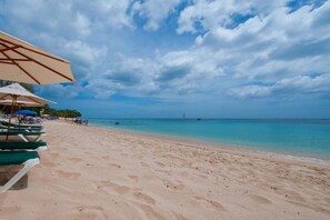 A beach with rows of sun loungers and umbrellas, a clear sky, and calm sea.