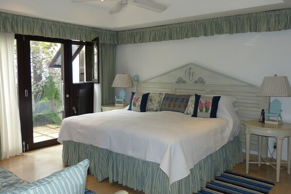 A bedroom with a large bed, a nightstand, a lamp, and a view of the outdoors through a sliding door.