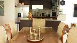 A modern kitchen with dark cabinetry, a stainless steel refrigerator, and a dining area with a glass table and wicker chairs. - SPACIOUS CORNER UNIT ON GROUND FLOOR (Paynes Bay)