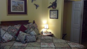 Une chambre à coucher avec une couvre-lit à motifs floraux, une lampe de chevet, un tableau encadré et des décorations murales comprenant un canard et un oiseau.