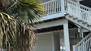 Una casa de dos pisos con un balcón, una palmera y dos parrillas en el porche.