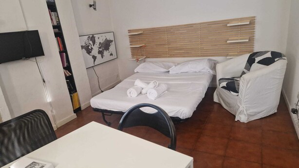 A hotel room with a bed, a chair, a table, a TV, and a world map on the wall. - Best location in Bologna. Studio equipped for long stays. SuperHost since 2011. (Bologna)