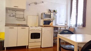 A compact kitchen with white appliances, a stove, oven, and a microwave. There's a small dining table and a chair. - Best location in Bologna. Studio equipped for long stays. SuperHost since 2011. (Bologna)