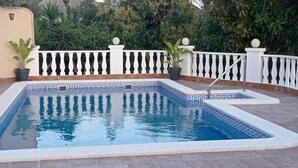 Ein rechteckiger Swimmingpool mit weiß-blauer Fliesenbordur, umgeben von einem weißen Zaun mit verzierten Balustraden und Kugelornamenten.