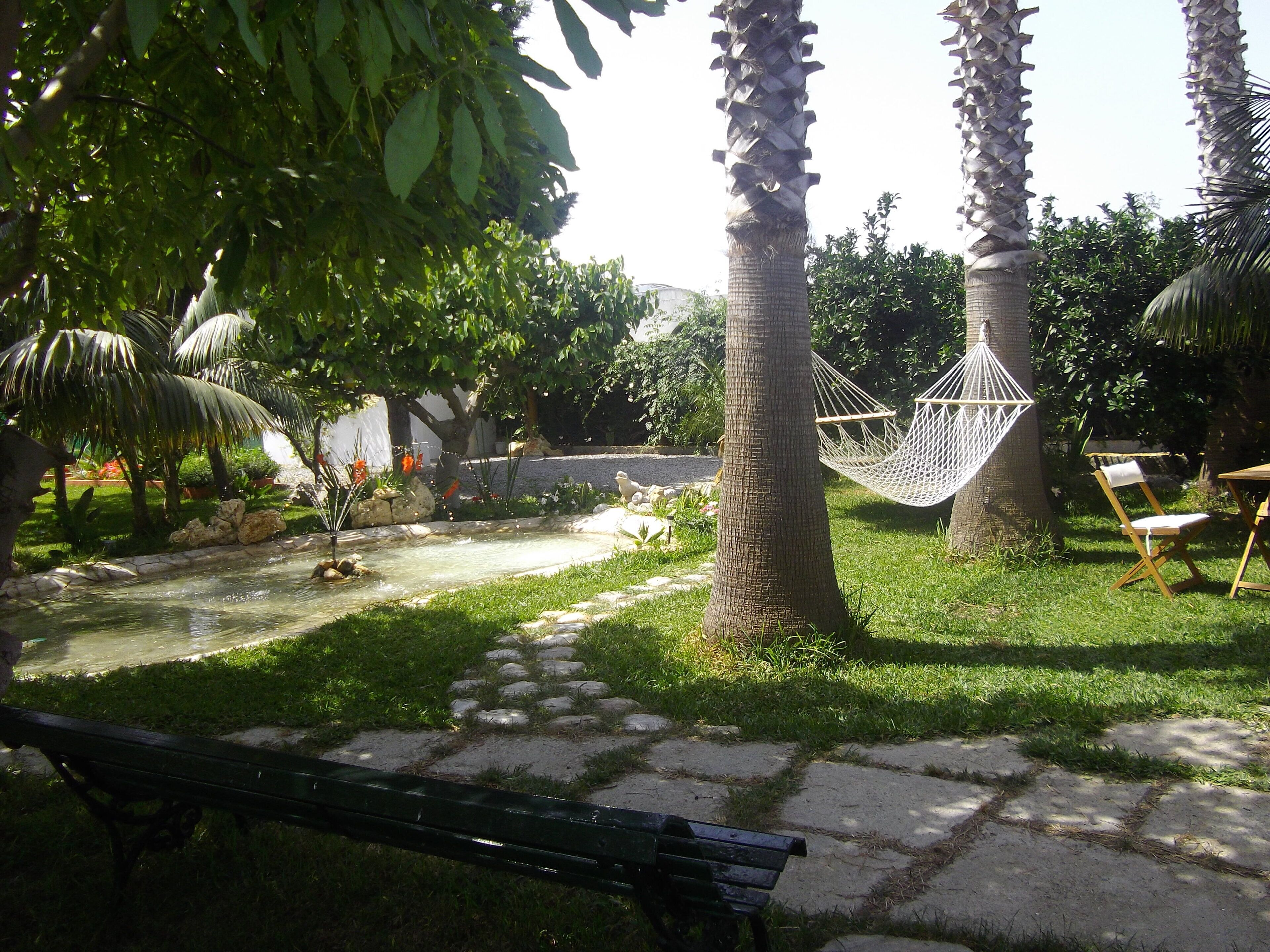 Un jardin avec un hamac, un banc et un petit étang.