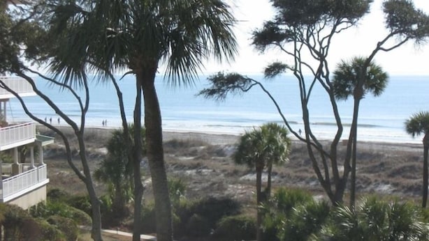 Ein direkt am Strand gelegenes Anwesen mit Blick auf den Ozean, Palmen und ein Gebäude mit einem Balkon, der den Strand überblickt.