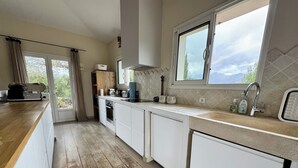 Een moderne keuken met witte kasten, een houten aanrechtblad en een groot raam met uitzicht op de omgeving.