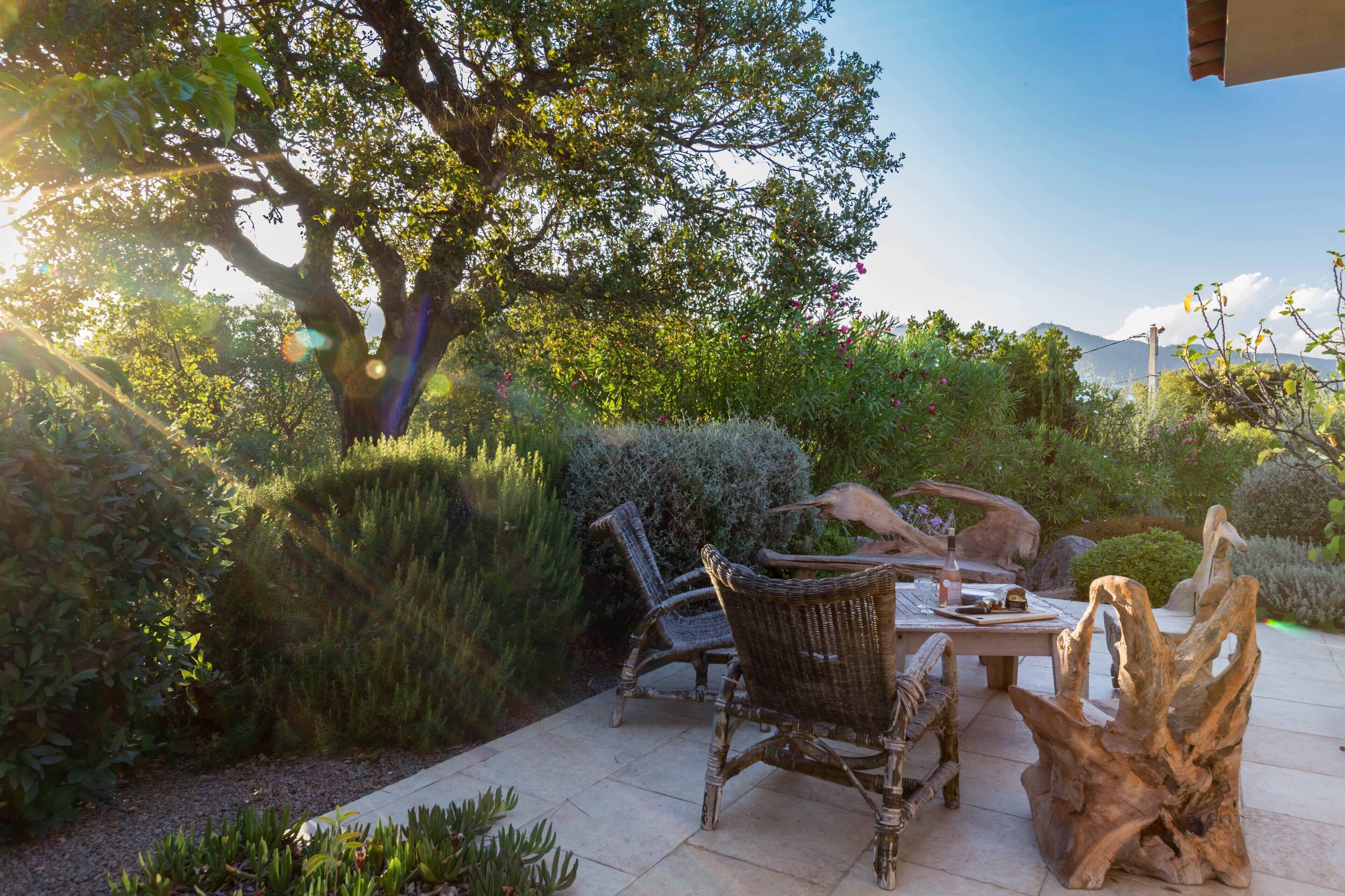 Eine Terrasse im Freien mit Korbmöbeln, einem Holztisch und einem großen Baum.