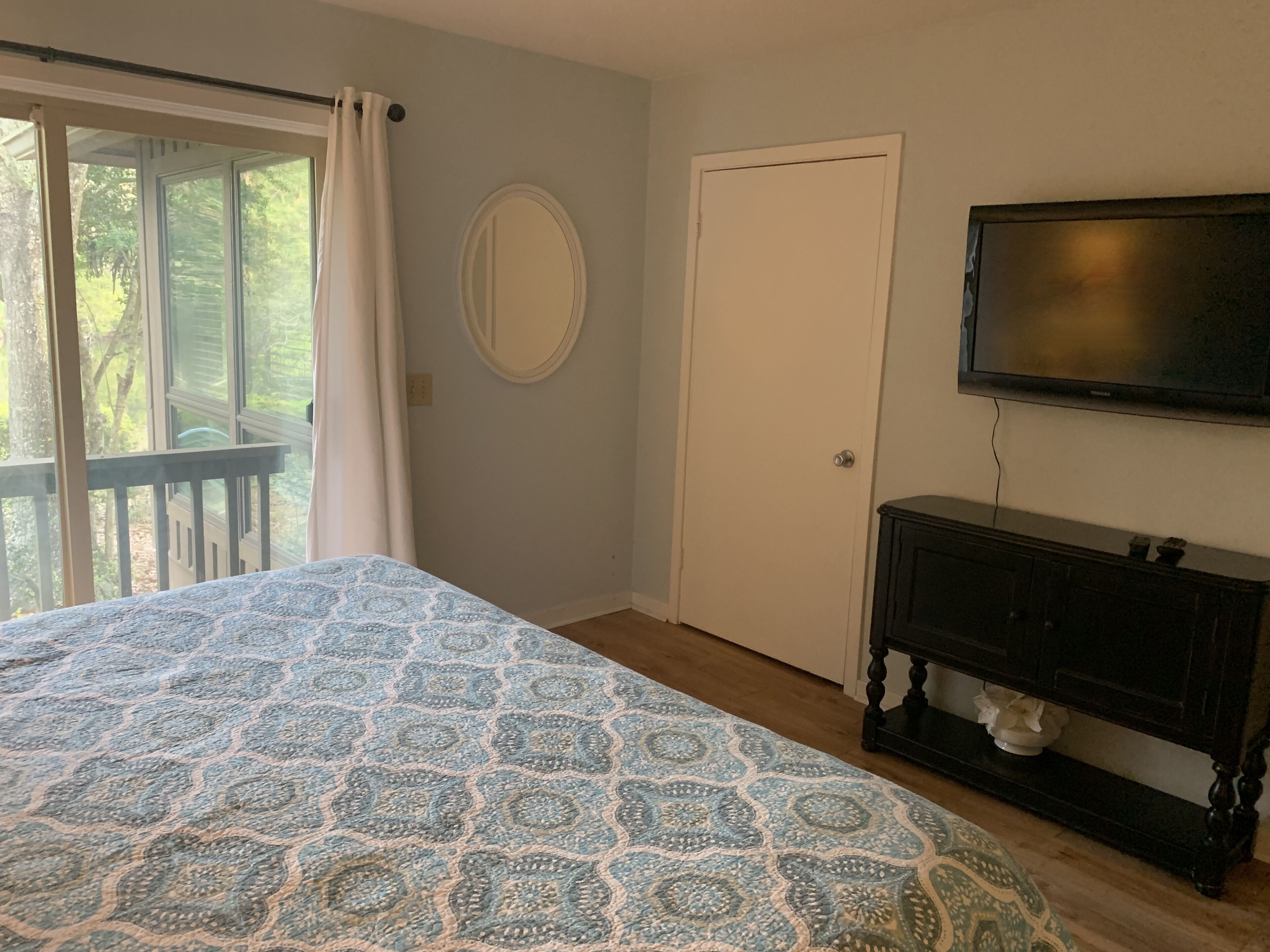 A bedroom with a bed, a television, a door, and a window with curtains.