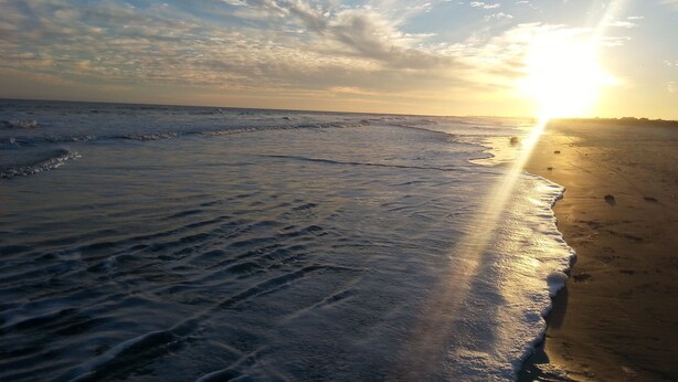 A beach with waves and a sunset.