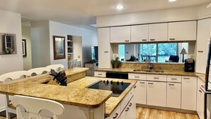 A modern kitchen with white cabinetry, a granite countertop, a built-in stove, and a large window offering a view of the outdoors.