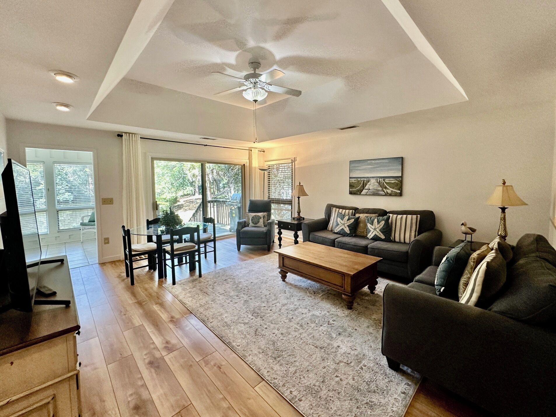 A spacious living room with a ceiling fan, a large window, a dining area, and a sofa set.