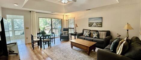 A spacious living room with a ceiling fan, a large window, a dining area, and a sofa set.