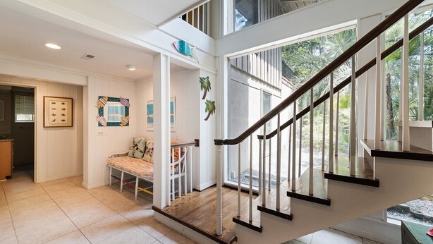 Un intérieur spacieux avec un escalier menant à un balcon, un coin repas et une vue sur l’extérieur.