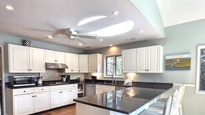 Une cuisine moderne avec des meubles blancs, un îlot central et un ventilateur de plafond.
