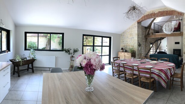 A spacious dining area with a wooden table set for four, a vase of flowers, and a view of the garden through large windows.
