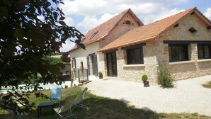 A stone building with a tiled roof, a gravel driveway, and a small garden area with chairs and a table.