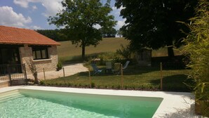 A rectangular swimming pool with clear water, surrounded by a stone wall and a grassy area with trees and a chair.