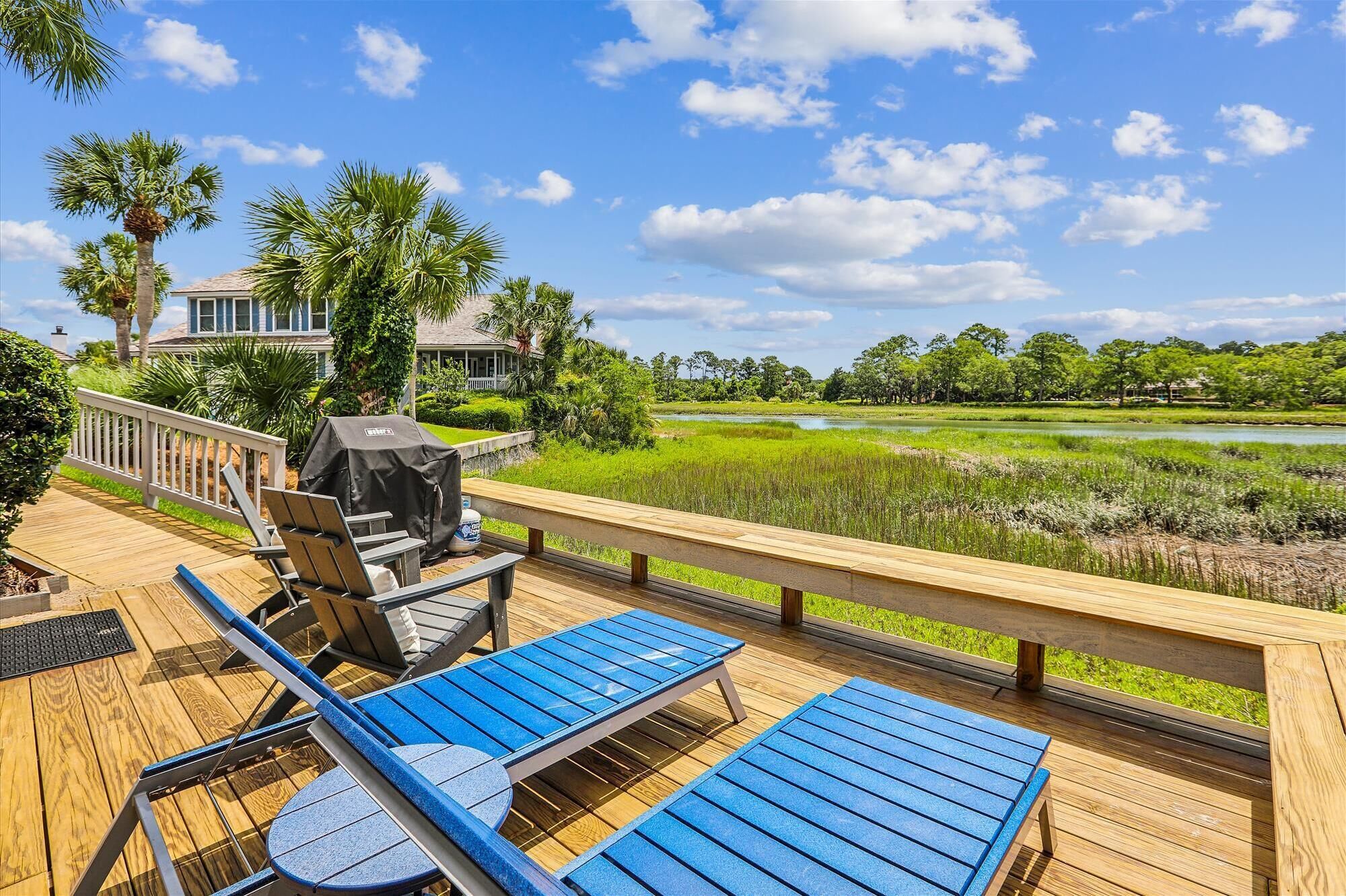 A deck with blue lounge chairs and a grill, overlooking a lush landscape and a golf course.