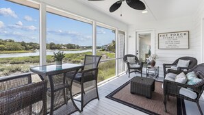 Eine überdachte Veranda mit Korbmöbeln, einem Deckenventilator und Blick auf einen See und Häuser.
