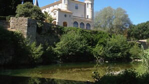 Um edifício que lembra um castelo, com duas torres, rodeado por vegetação e um corpo de água.