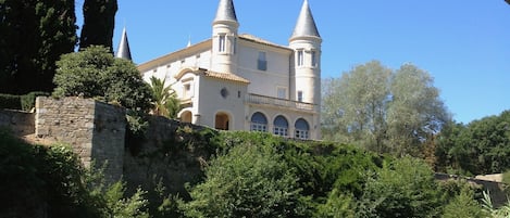 A castle-like building with two towers, surrounded by greenery and a body of water.