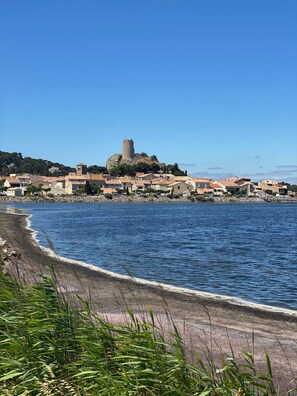 Eine Küstenstadt mit einem markanten Turm auf einem Hügel, einem Strand mit Wellen und Gebäuden mit roten Ziegeldächern.