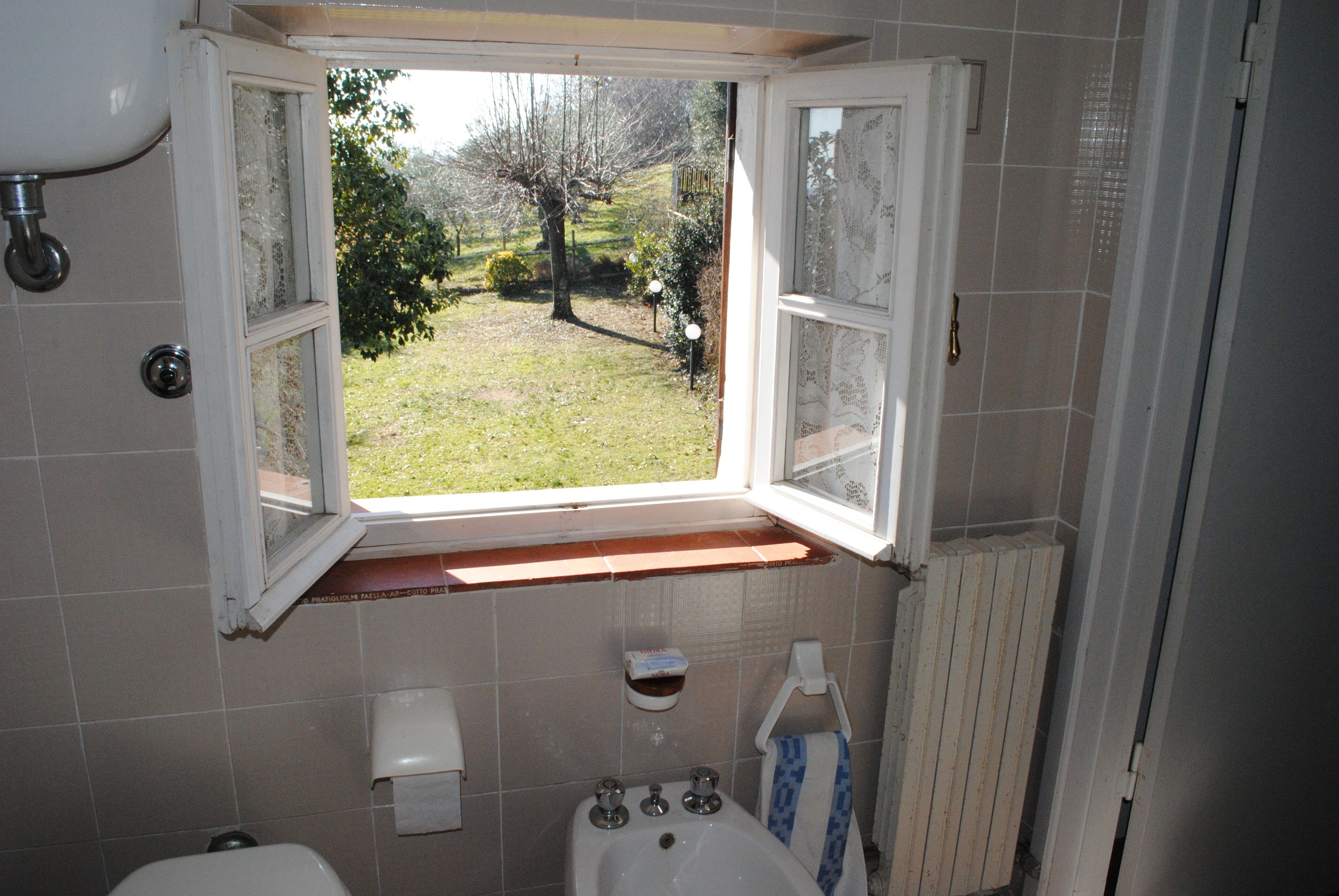 A bathroom with a window, a toilet, a sink, and a towel rack.