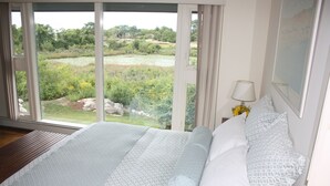 A bedroom with a large window, a bed with patterned bedding, a bedside lamp, and a framed picture on the wall. - Beautiful Oceanfront Home in Estate Setting Gloucester — FALL RENTAL AVAILABLE! (Gloucester)