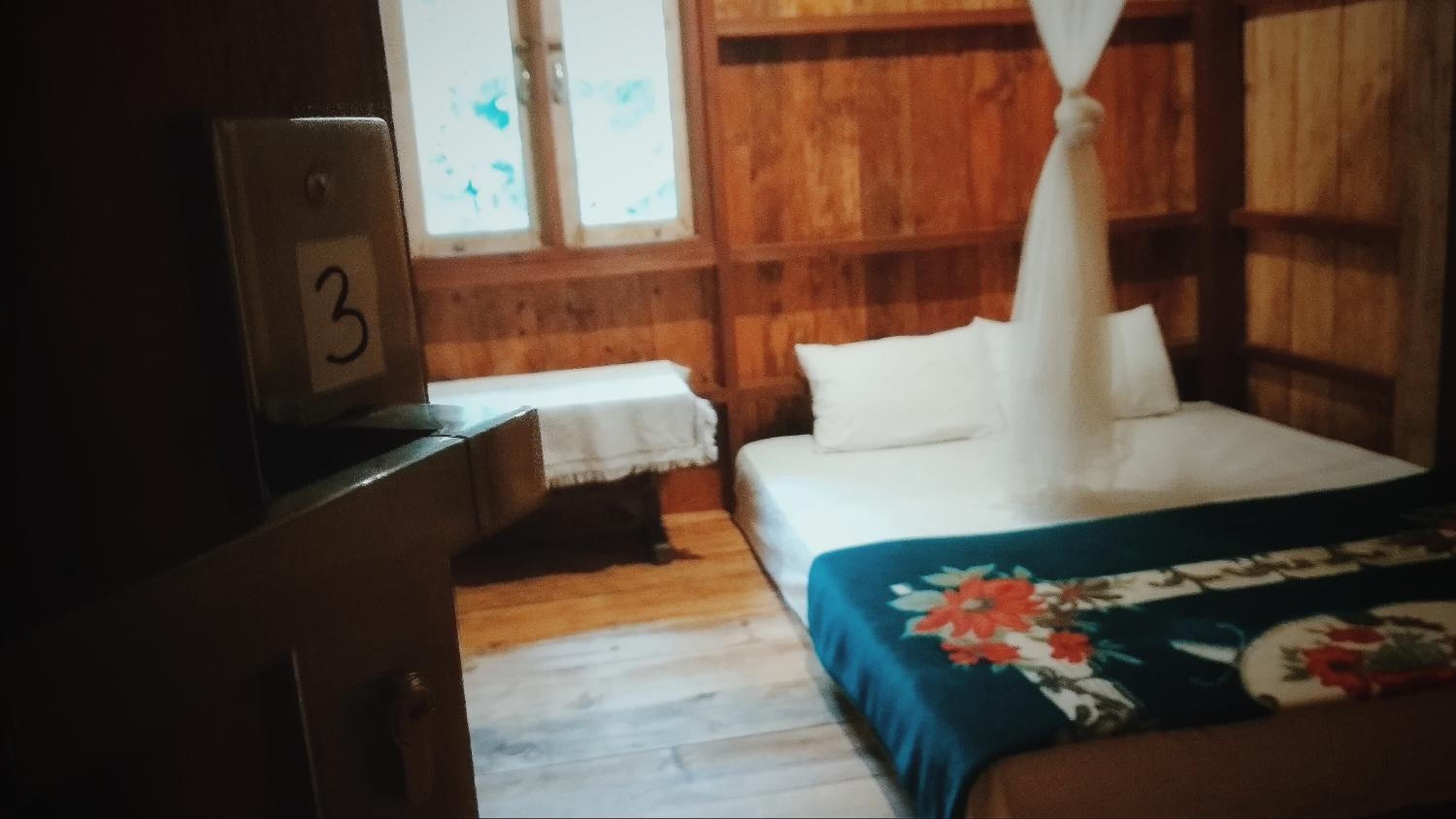 A room with a bed, a nightstand, a wooden dresser, and a window with a curtain.