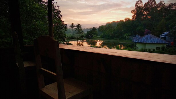 Une terrasse en bois surplombe un lac paisible, avec une petite maison en arrière-plan.
