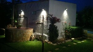 A small, single-story building with a stone facade and a flat roof. There are three exterior lights mounted on the building, and a small garden area with a stone planter and a metal sculpture. - COUNTRY HOUSE IMMERSED IN A LEMONET 2 km from the sea and Noto - Wifi - climate (noto)