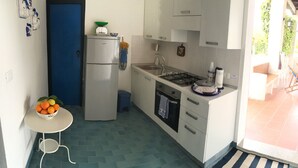 A compact kitchen with a refrigerator, stove, sink, and a small table with a bowl of fruit. - COUNTRY HOUSE IMMERSED IN A LEMONET 2 km from the sea and Noto - Wifi - climate (noto)