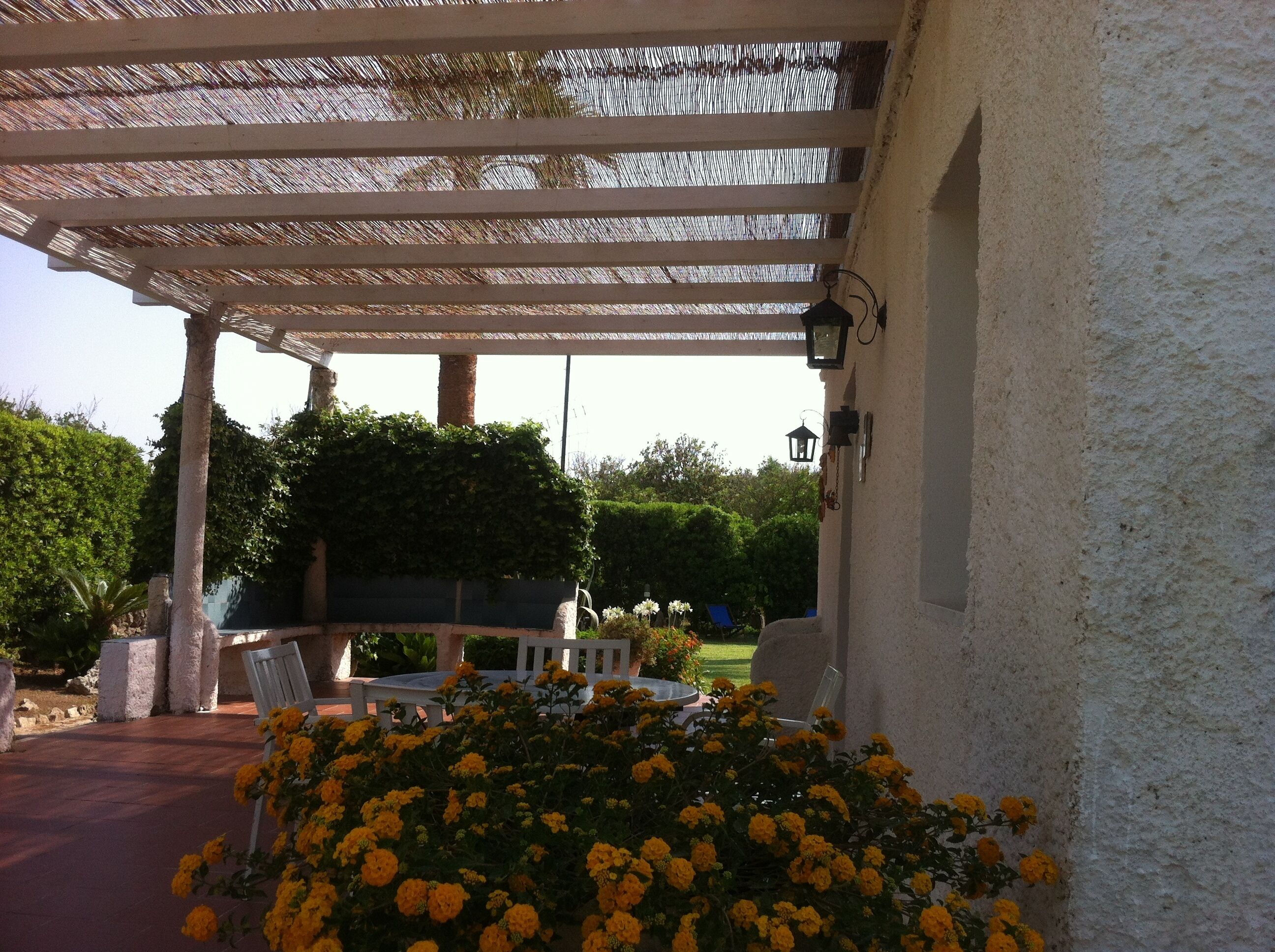 A covered outdoor area with a pergola, seating, and a wall-mounted light fixture.