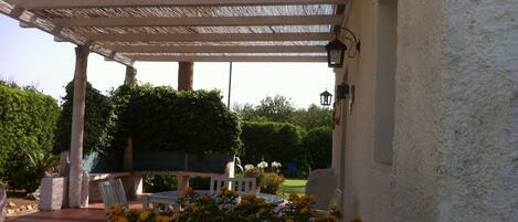 A covered outdoor area with a pergola, seating, and a wall-mounted light fixture.