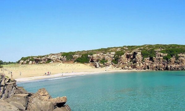 Ein Küstenstrand mit klarem Wasser, felsigen Klippen und einem sandigen Ufer.