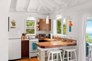Una cocina con isla de madera, armarios blancos, estufa a gas y vistas al exterior.