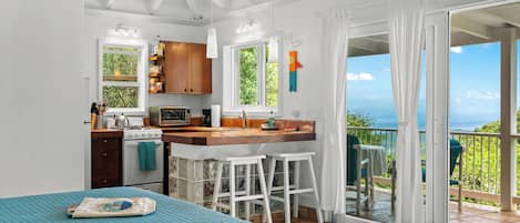 A compact kitchen with a dining area, a large window, and a view of the sea.