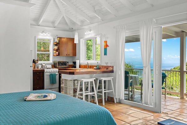 A compact kitchen with a dining area, a large window, and a view of the sea.