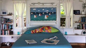 A bedroom with a bed, a window with a view of sailboats, bookshelves, and a plant. - Sea Cottage - Charming and Romantic with a Stunning View (St. John)