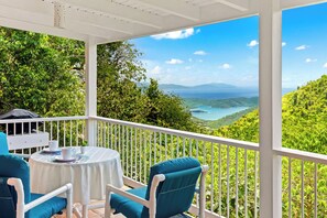 Un balcone con tavolo e sedie, affacciato su un paesaggio pittoresco ricco di verde e vista sul mare.
