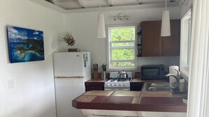 A kitchen with a white refrigerator, a gas stove, a sink, and a window with a view of greenery. There are two white stools and a painting on the wall. - Sea Cottage - Charming and Romantic with a Stunning View (St. John)