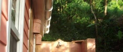 Een kleine hottub buiten, vastgemaakt aan een huis met een raam en een bloempot.